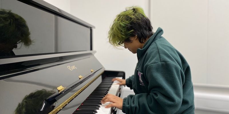 A student playing an upright piano