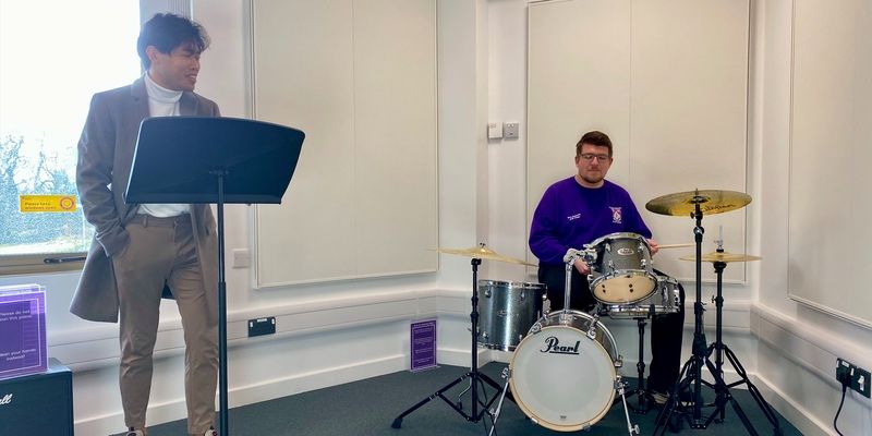 Two students using the music room, one singing and the other playing drums