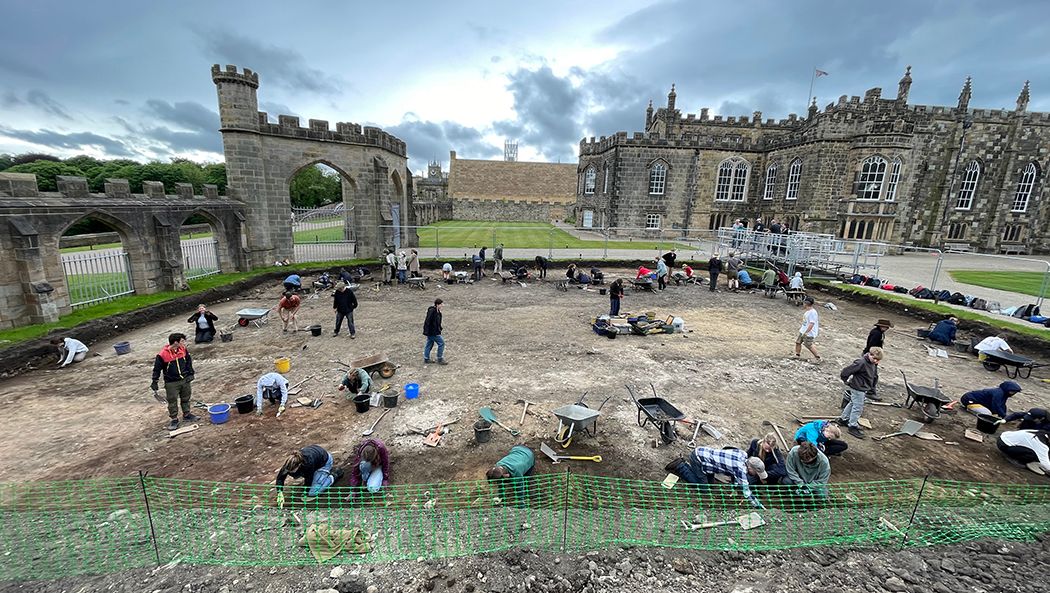 People digging in an archaeological excavation, with archways and a castle behind