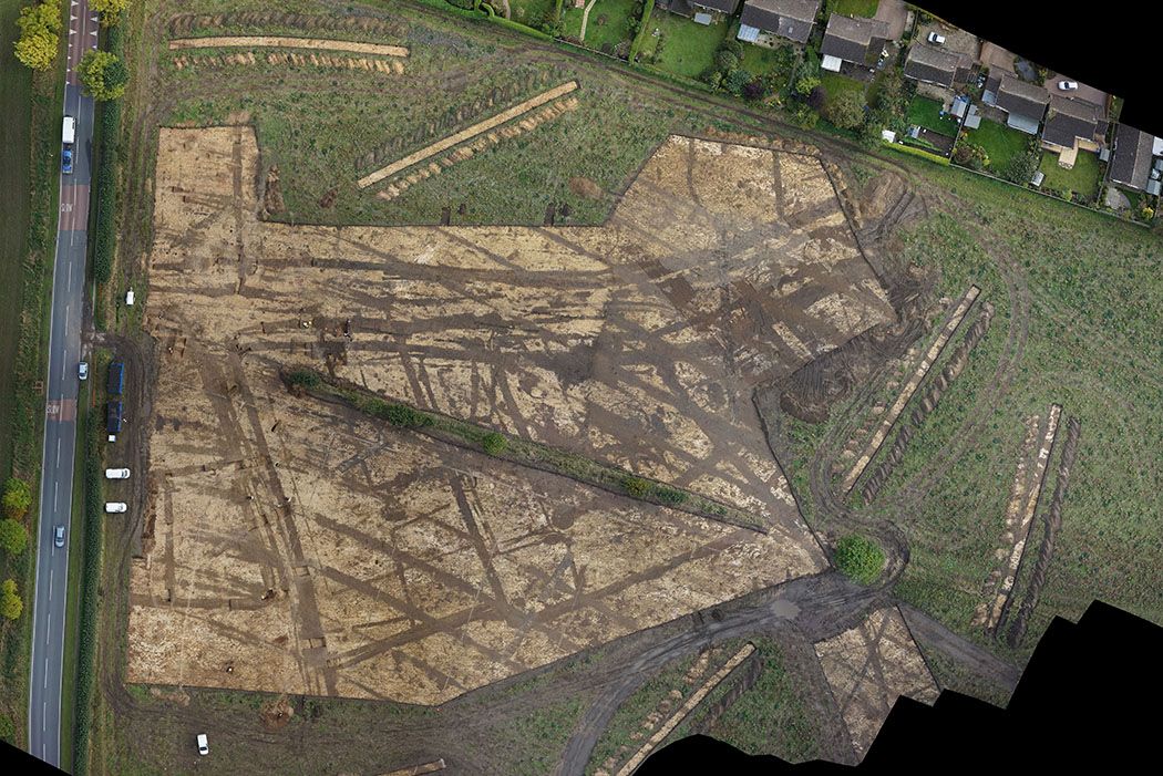 Overview of an excavation area surrounded by trenches with the features of a Romano-British settlement in dark brown against the lighter natural soil