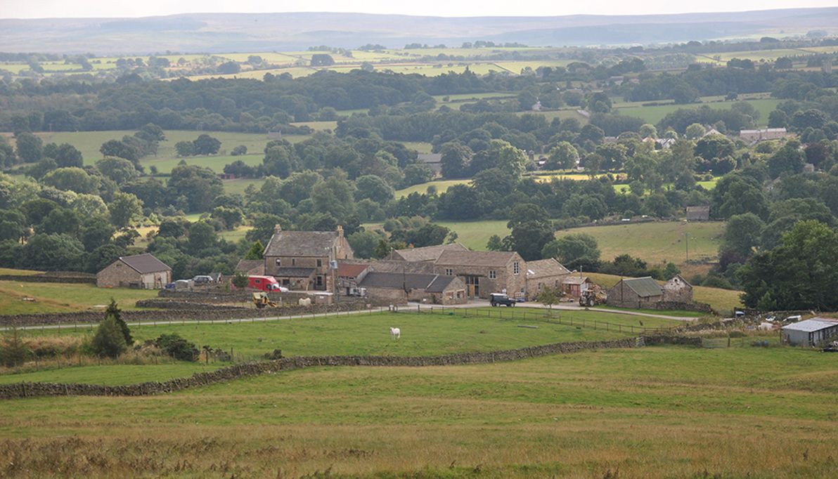 a photograph of typical northern English pastoral farmland with an old farm yard in the middle-distance and the Pennine Hills beyond