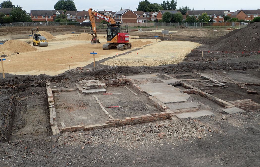 The foundations of an excavated building, with a housing estate under construction behind