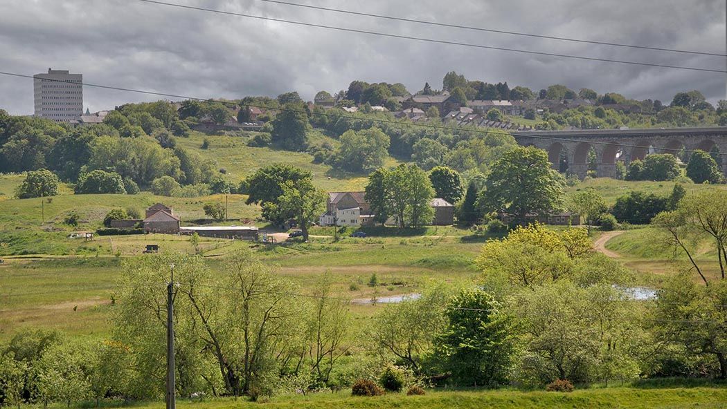 A farm in County Durham seen in the valley bottom, with a viaduct and buildings behind