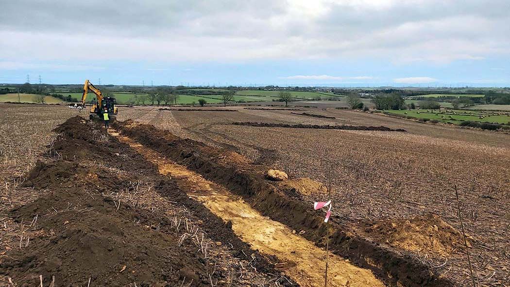 An archaeologist watching a JCB excavate a trench