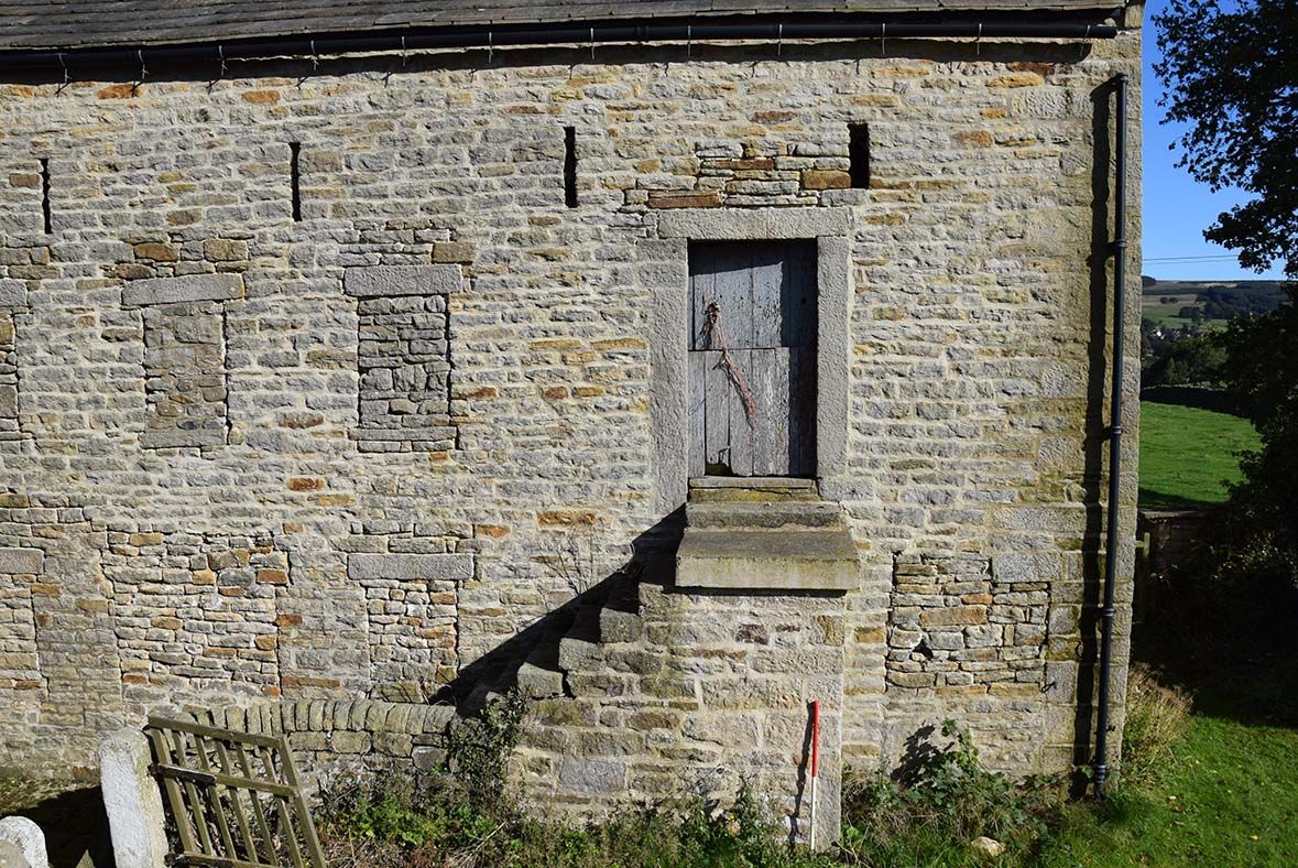 Derelict farm building with red and white ranging rod leaning against the wall