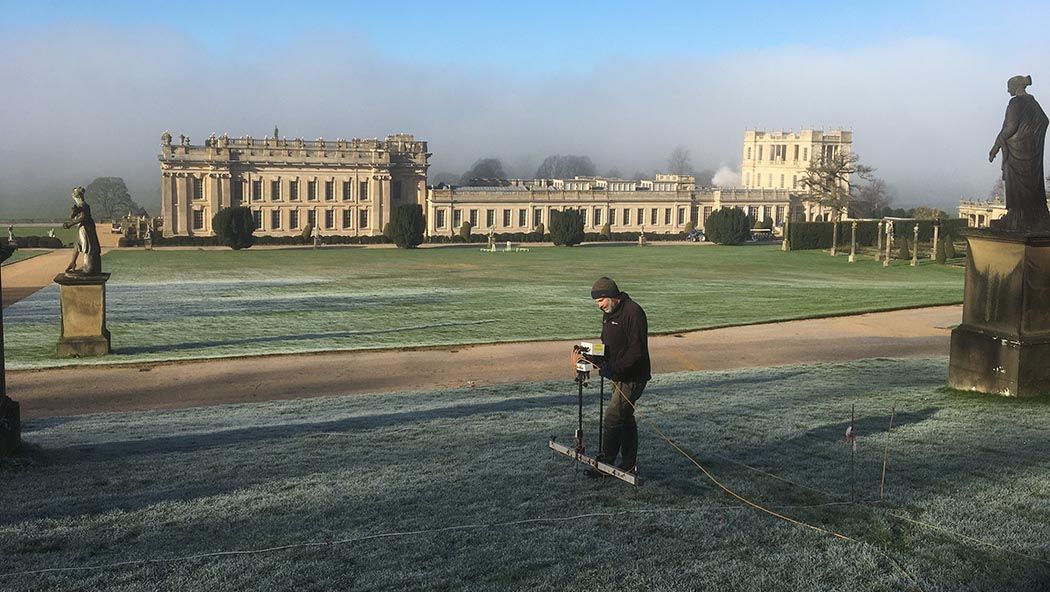 an archaeologist placing earth-electric resistance probes into a frosty lawn outside a stately home