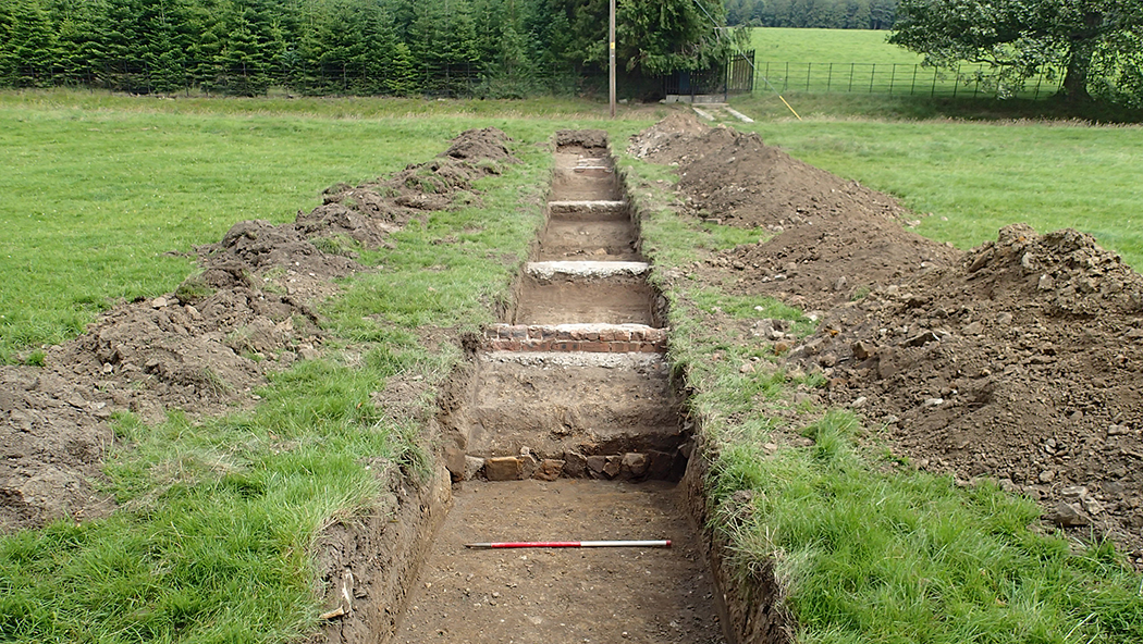 Field with an excavated trench showing a series of walls and features which have been uncovered