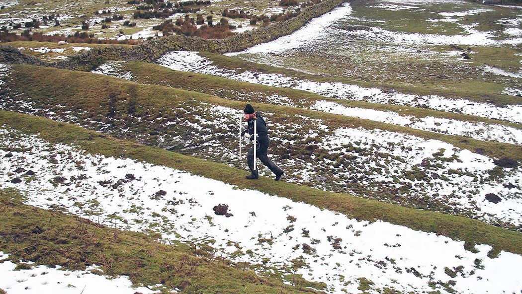 Someone doing magnetometer survey over the ramparts of a Roman fort in the snow