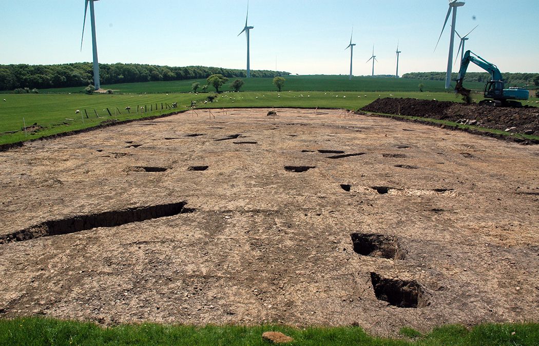 Excavated sections of ditches of a roman settlement with wind turbines and digger in background