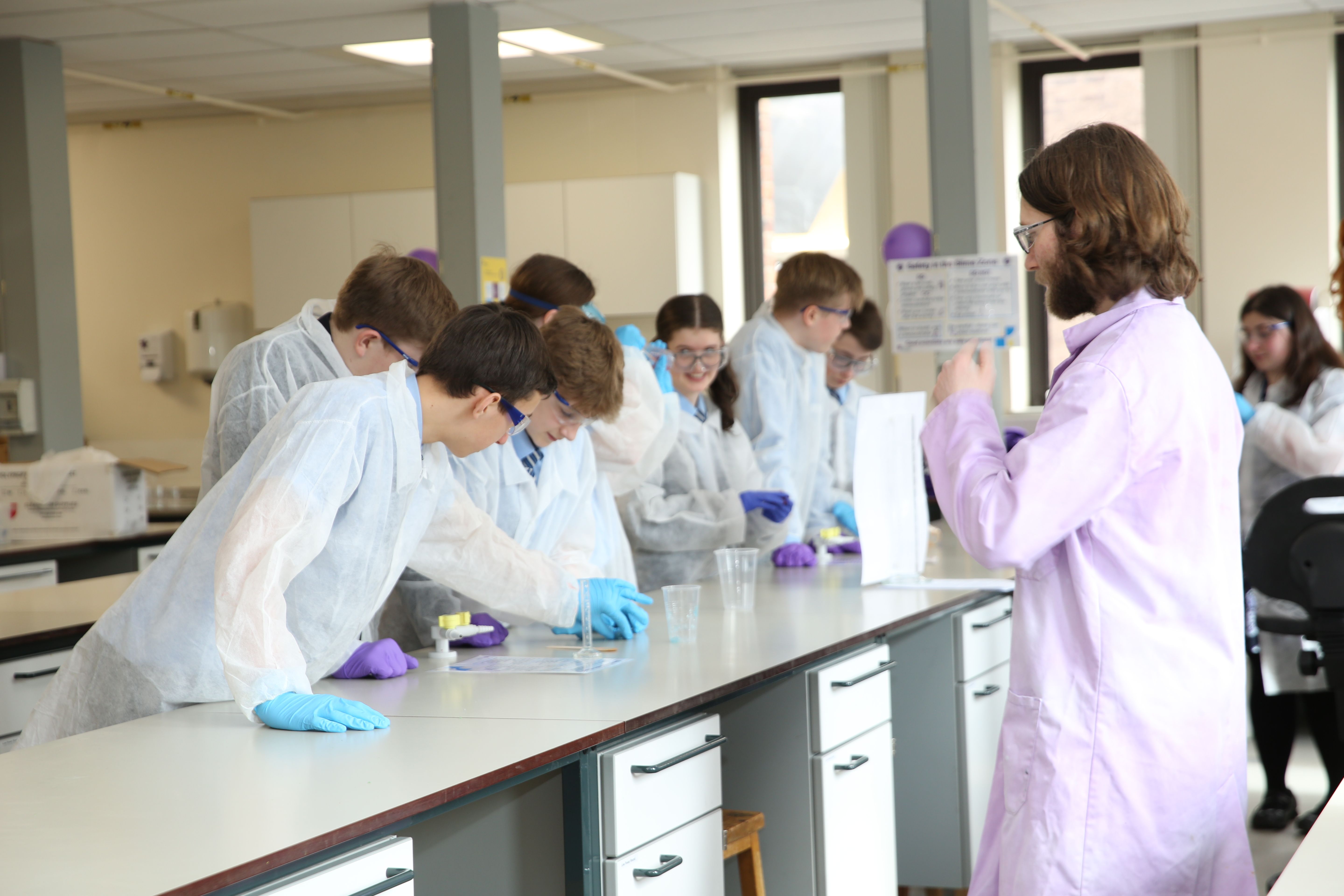 Group of teenage students in lab coats with tutor in lab coat doing a lab bench based science experiment
