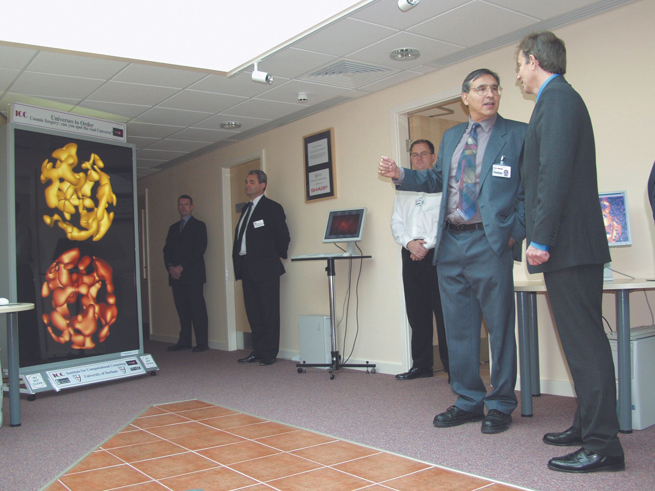 Carlos Frenk with Tony Blair in the Ogden Centre East building, with some cosmological simulated images on a big display board