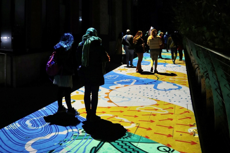 People walking over a coloured art projection on the floor