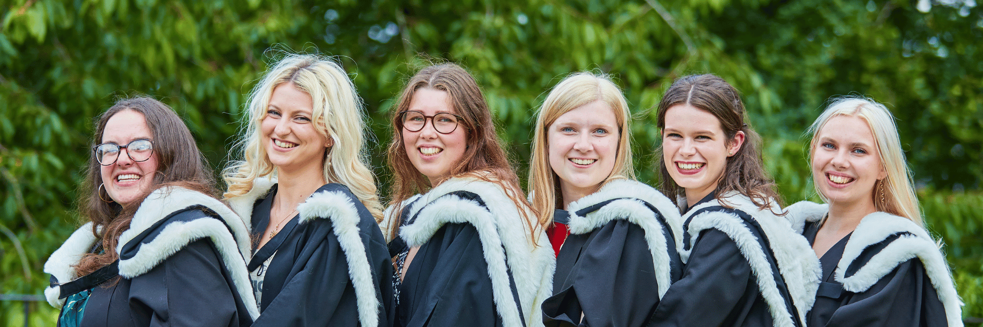 A group of students in gowns smiling standing behind one another