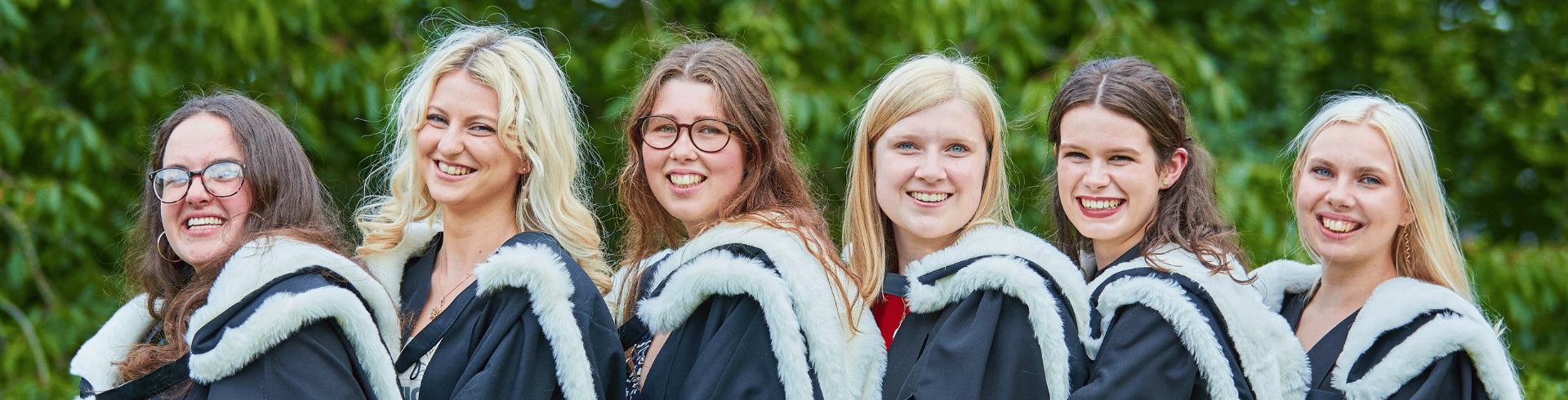 A group of students in gowns standing behind one another smiling