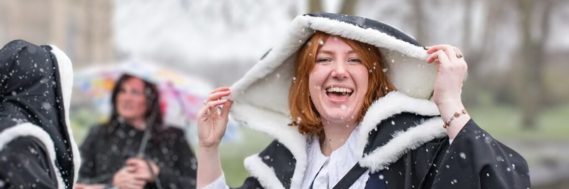 A student holding the hood of a graduation gown with flurries of snow