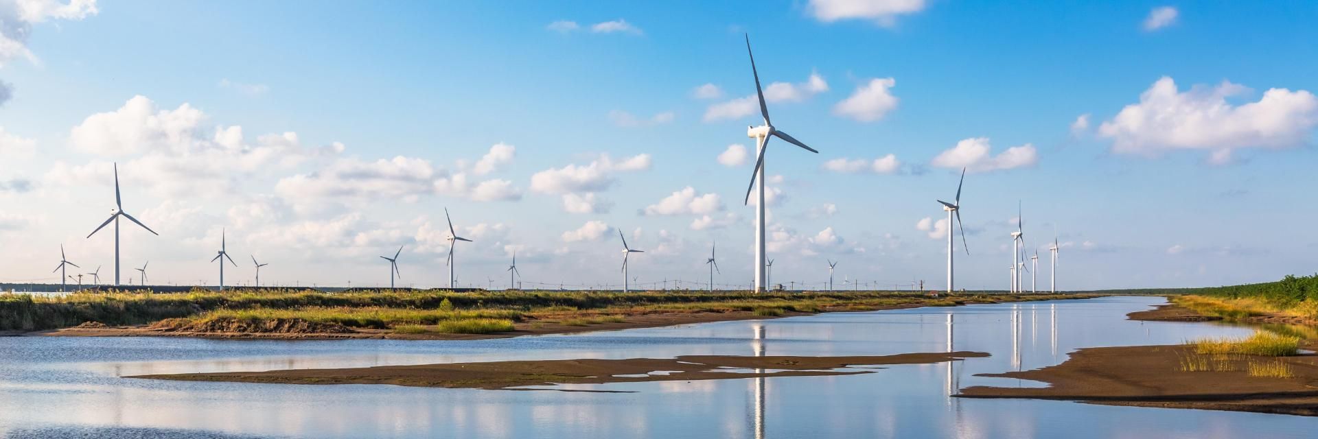 Wind turbines against a blue sky reflected in ground water