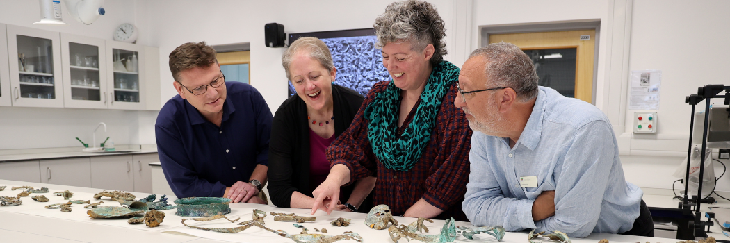 Four colleagues stand at a table with Melsonby artefacts spread around