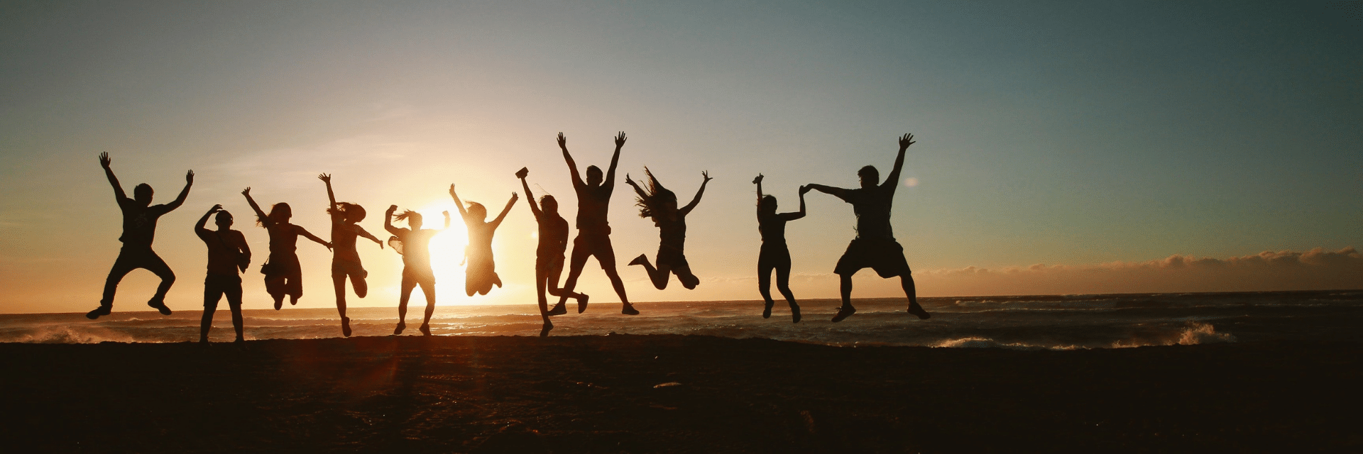 A group of people jumping in the air on the beach silhouetted