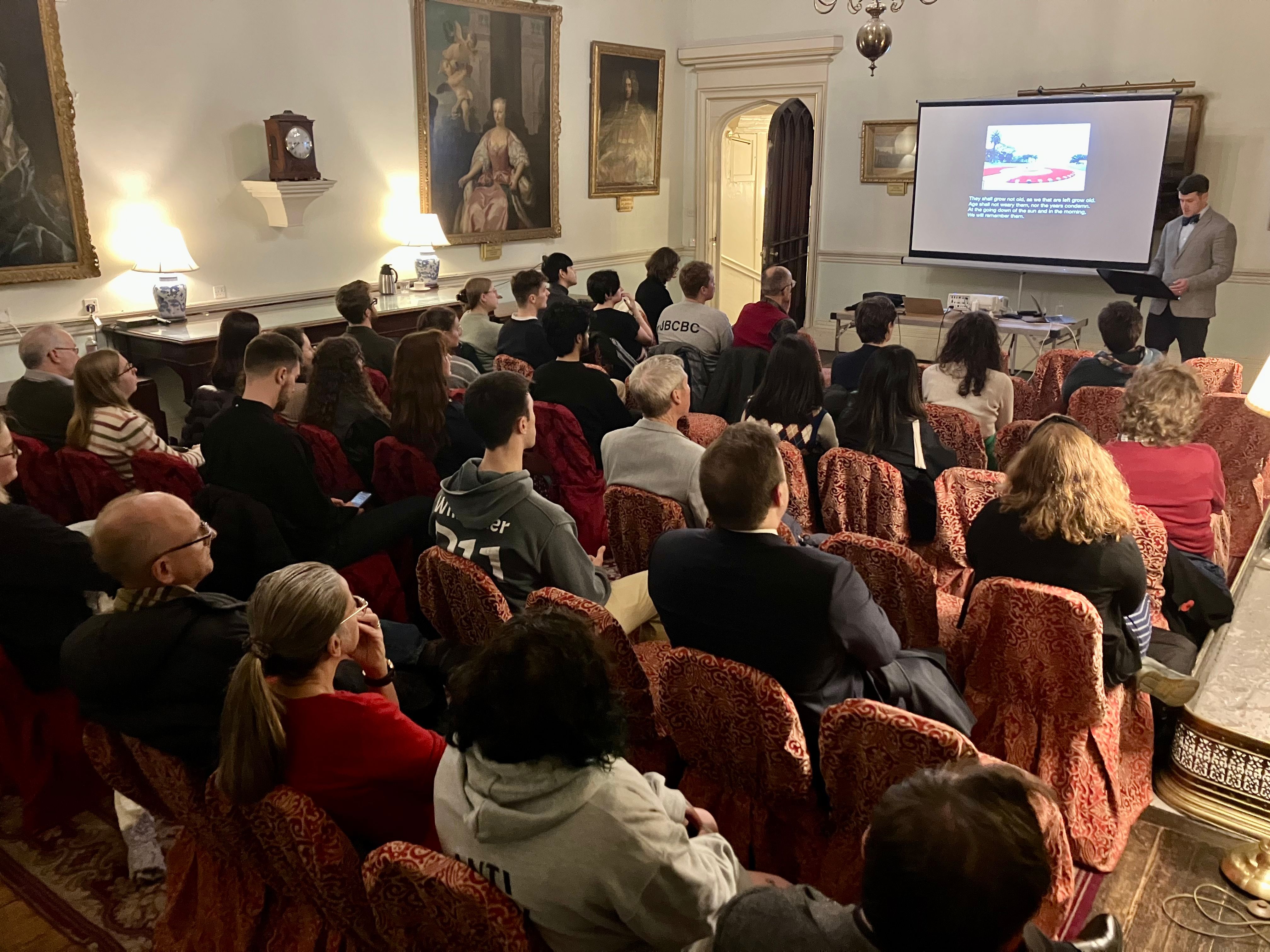 Around 35 people sitting in a grand room looking at a man giving a lecture