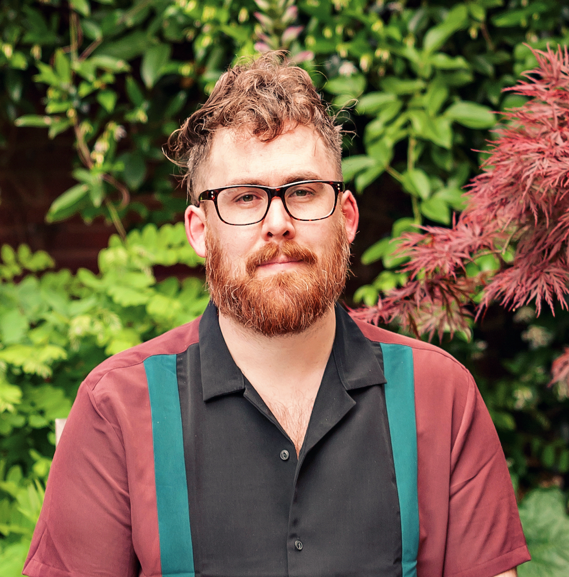 A man with a beard in front of a garden